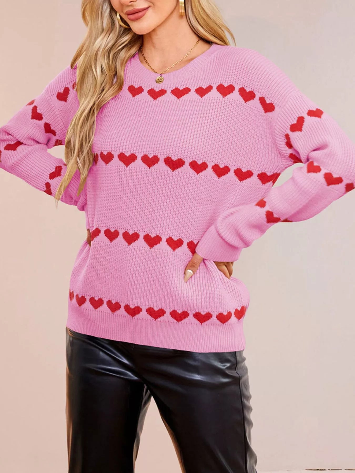 On-model front view of a pink dropped shoulder sweater with rows of red hearts