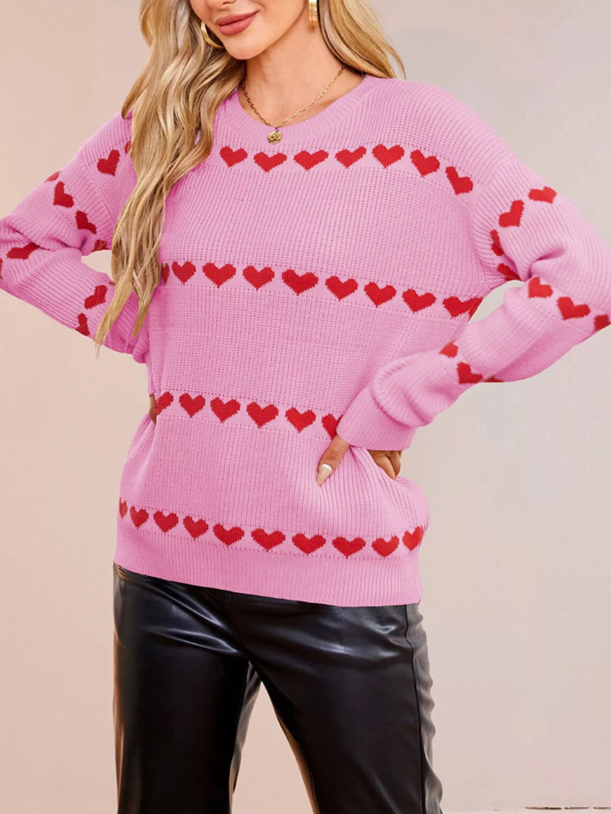 On-model front view of a pink dropped shoulder sweater with rows of red hearts