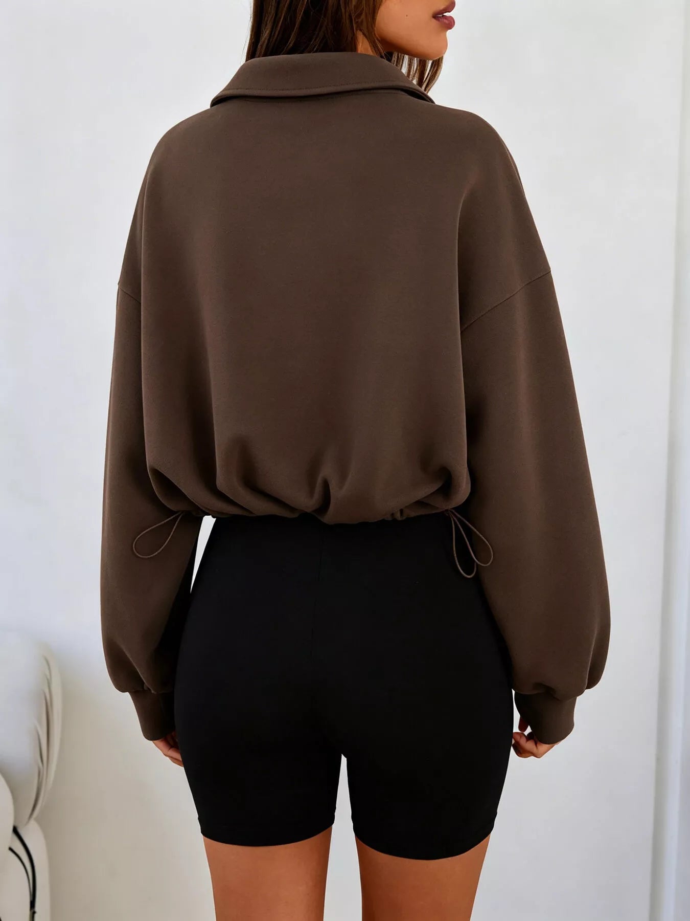 Back view of brown half zip sweatshirt with drawstring hem and relaxed fit