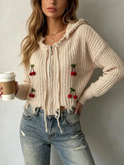 Apricot knit zip up hooded sweater with red cherry appliques worn on model holding coffee
