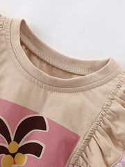 Close-up of the tan top neckline and gathered ruffle shoulder with pink pom trim