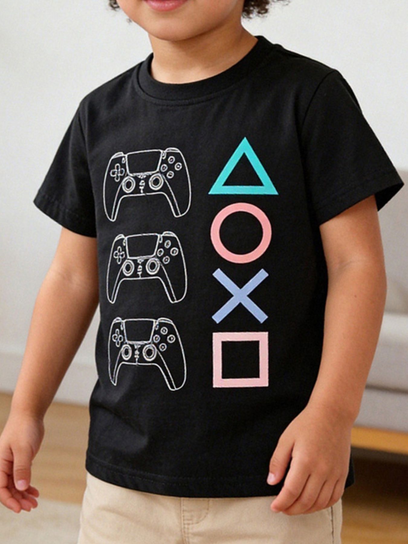 Black children's round neck T-shirt with white game controller outlines and colorful geometric shapes, front view