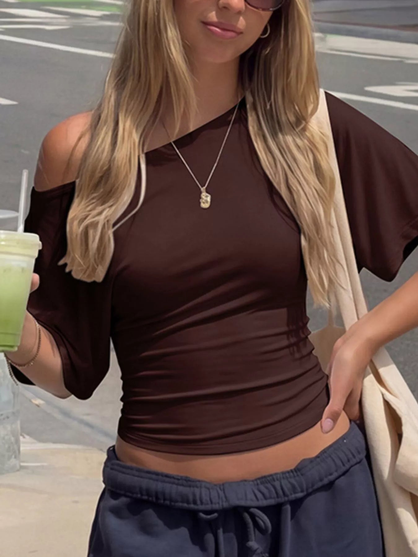 Close-up lifestyle view of a dark brown boat-neck short-sleeve T-shirt with relaxed draping and ruched side details