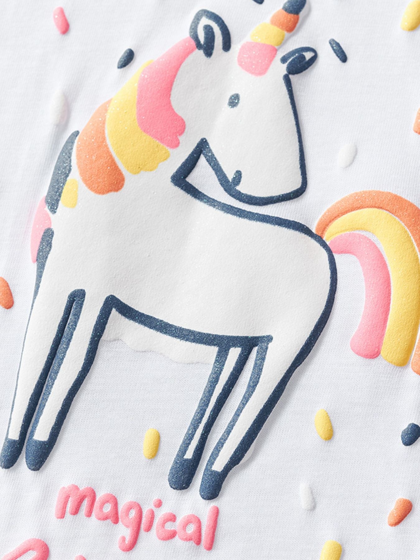 Close view of the white children's tee unicorn graphic with a rainbow mane tail and confetti dots