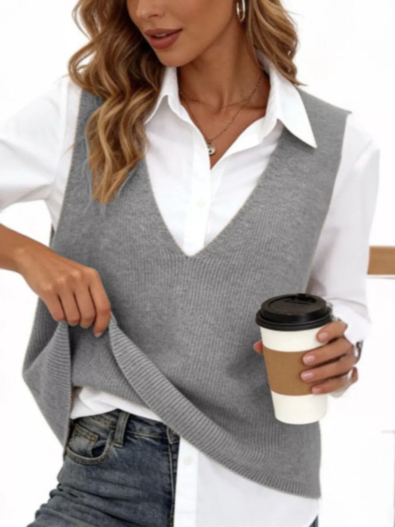 Gray V neck knit sweater vest over white shirt, model holding coffee and lifting hem