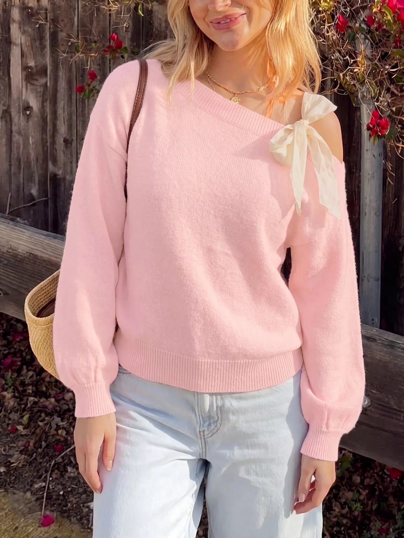 Front view of a pink one-shoulder sweater with a large cream bow at the shoulder