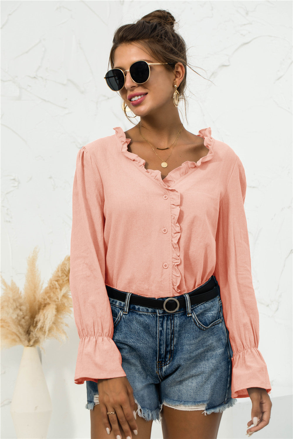 Front view of a peach frill-trim V-neck shirt with flounce sleeves, styled with denim shorts and a black belt