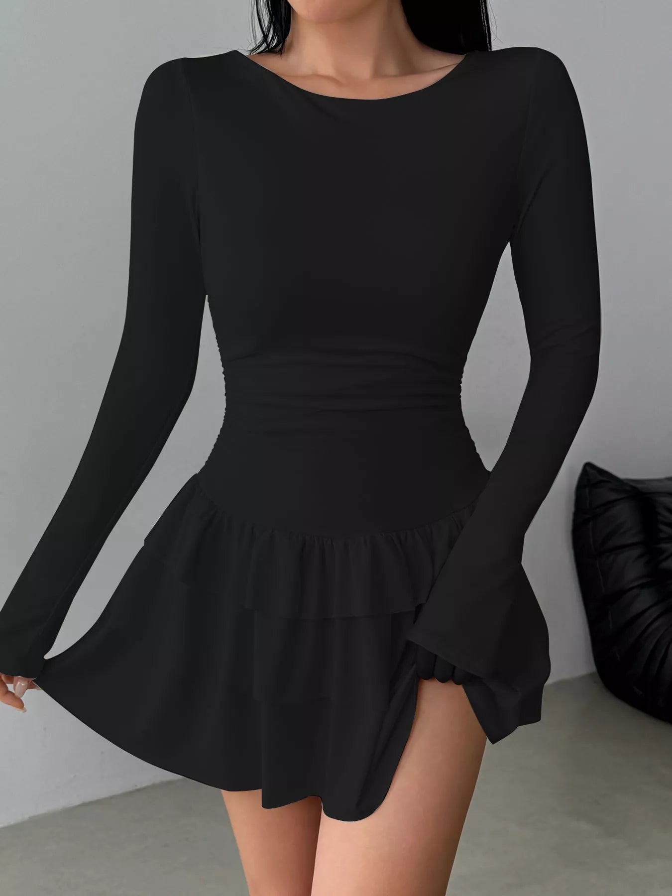 Black long sleeve mini dress worn front facing while holding out the tiered ruffle skirt