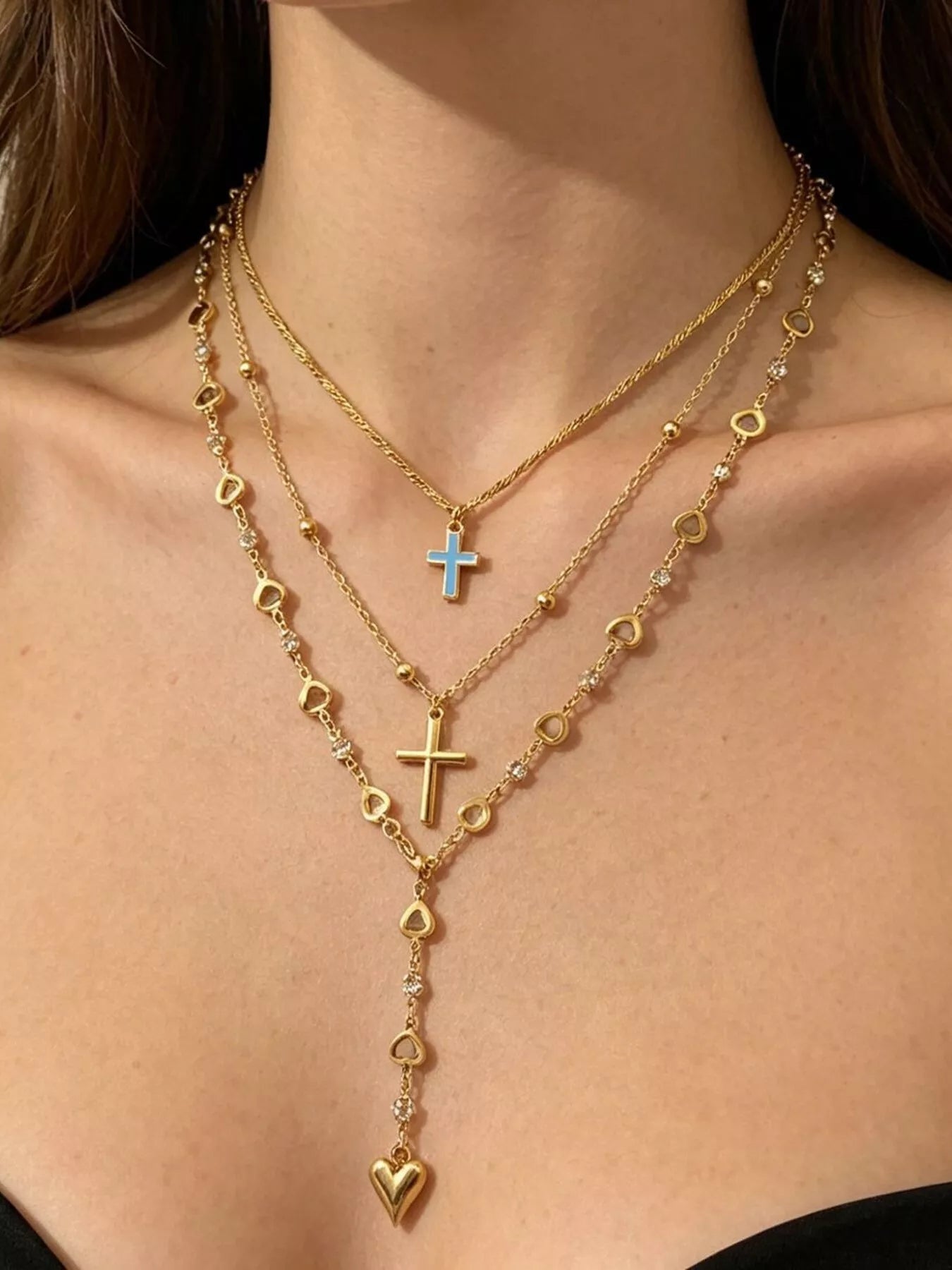 Layered gold necklaces worn on model with blue cross, gold cross and heart drop pendant