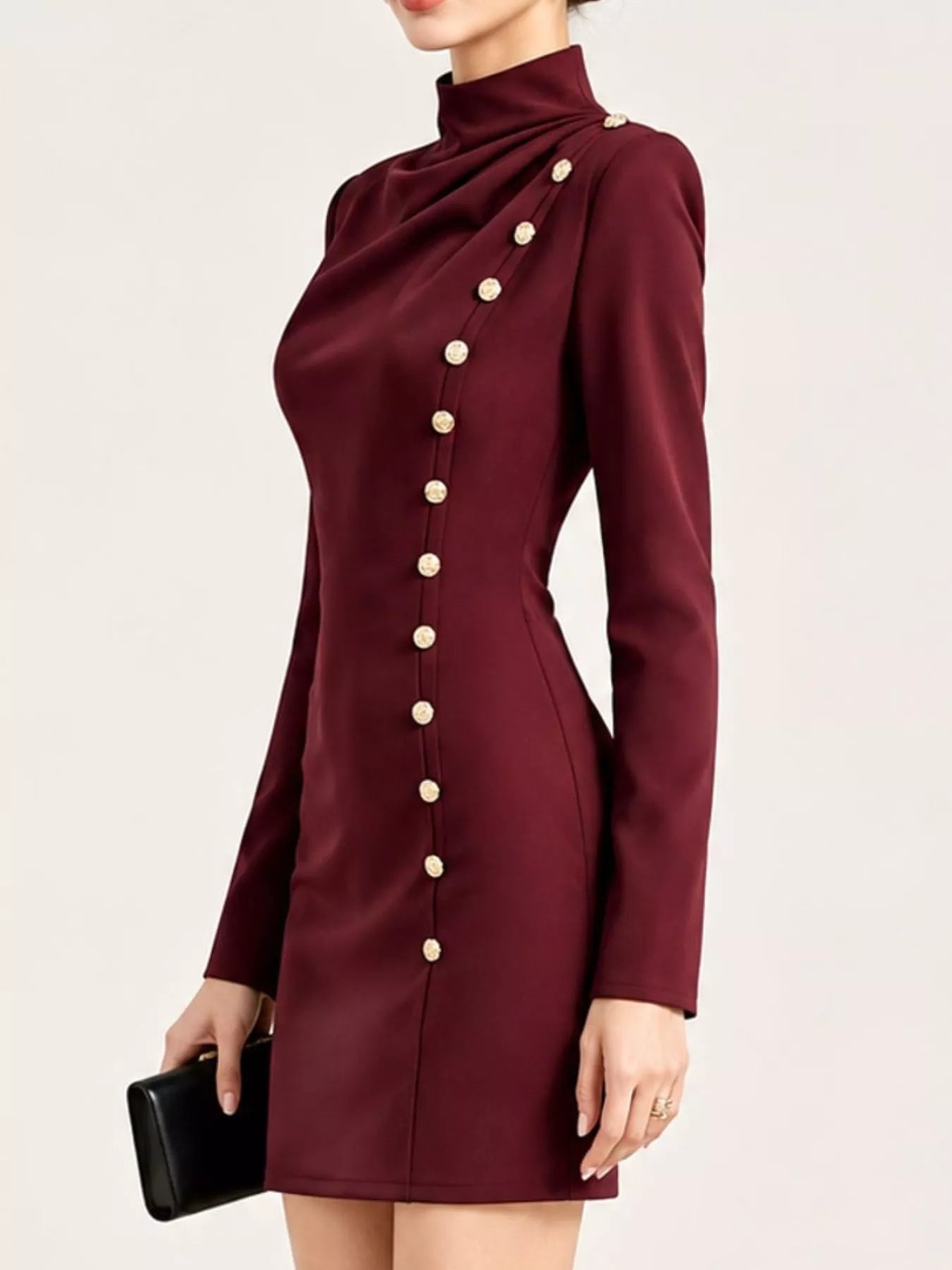 Side view of model in studio wearing burgundy mock neck mini dress with gold decorative buttons