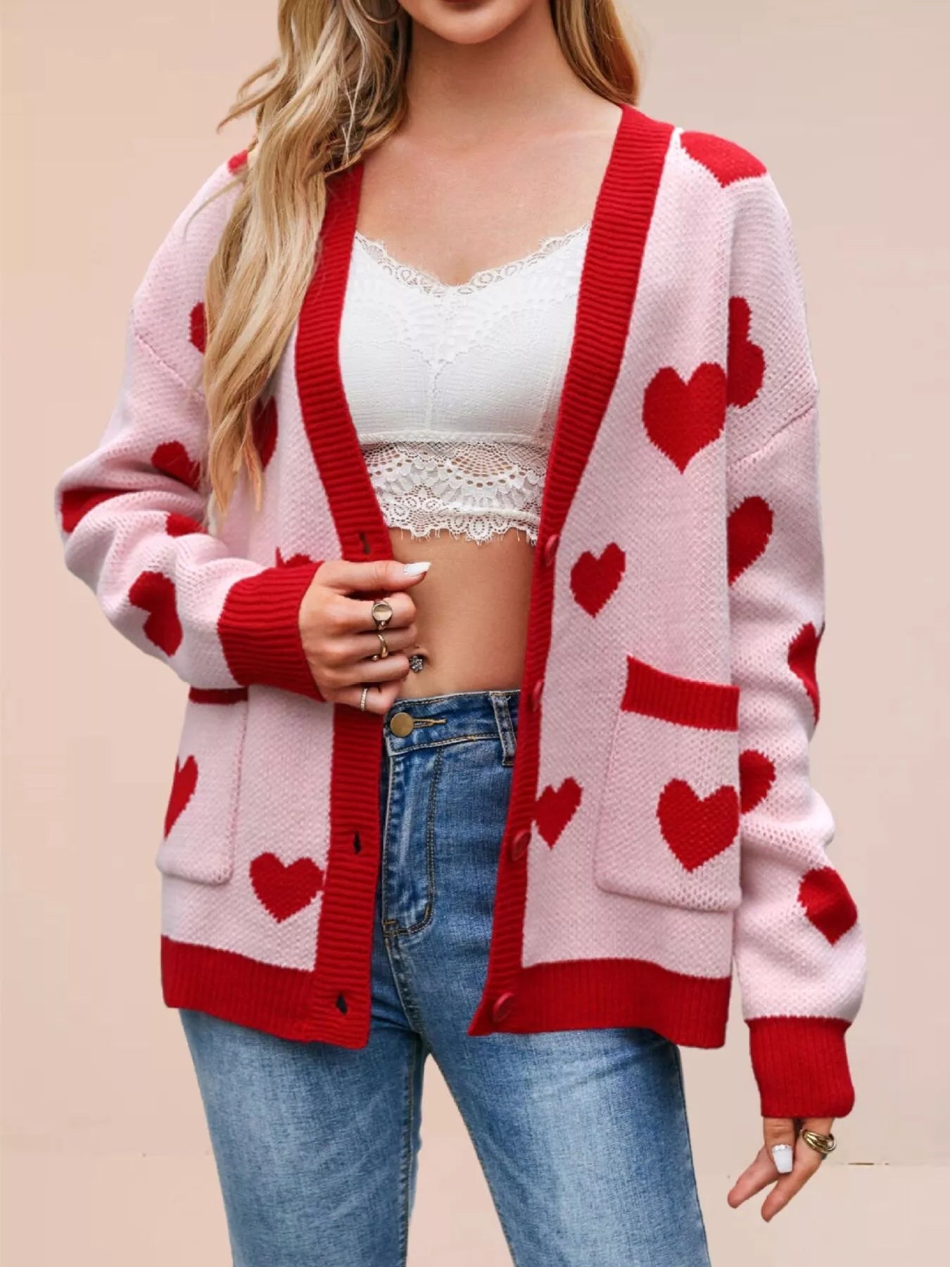 Pink knit cardigan with red hearts worn open over a white lace top