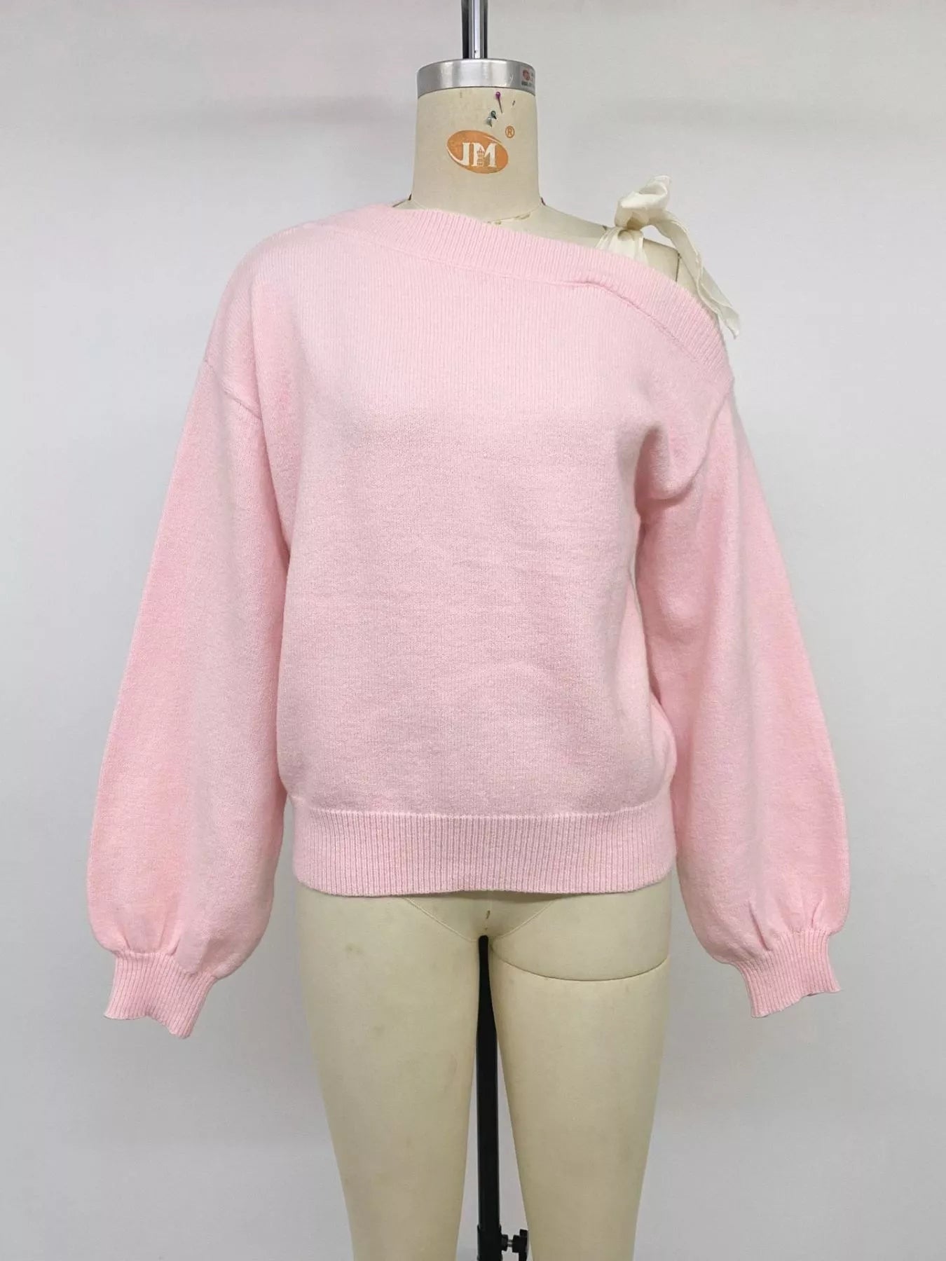 Front view of a pink one-shoulder sweater with a cream bow on a mannequin