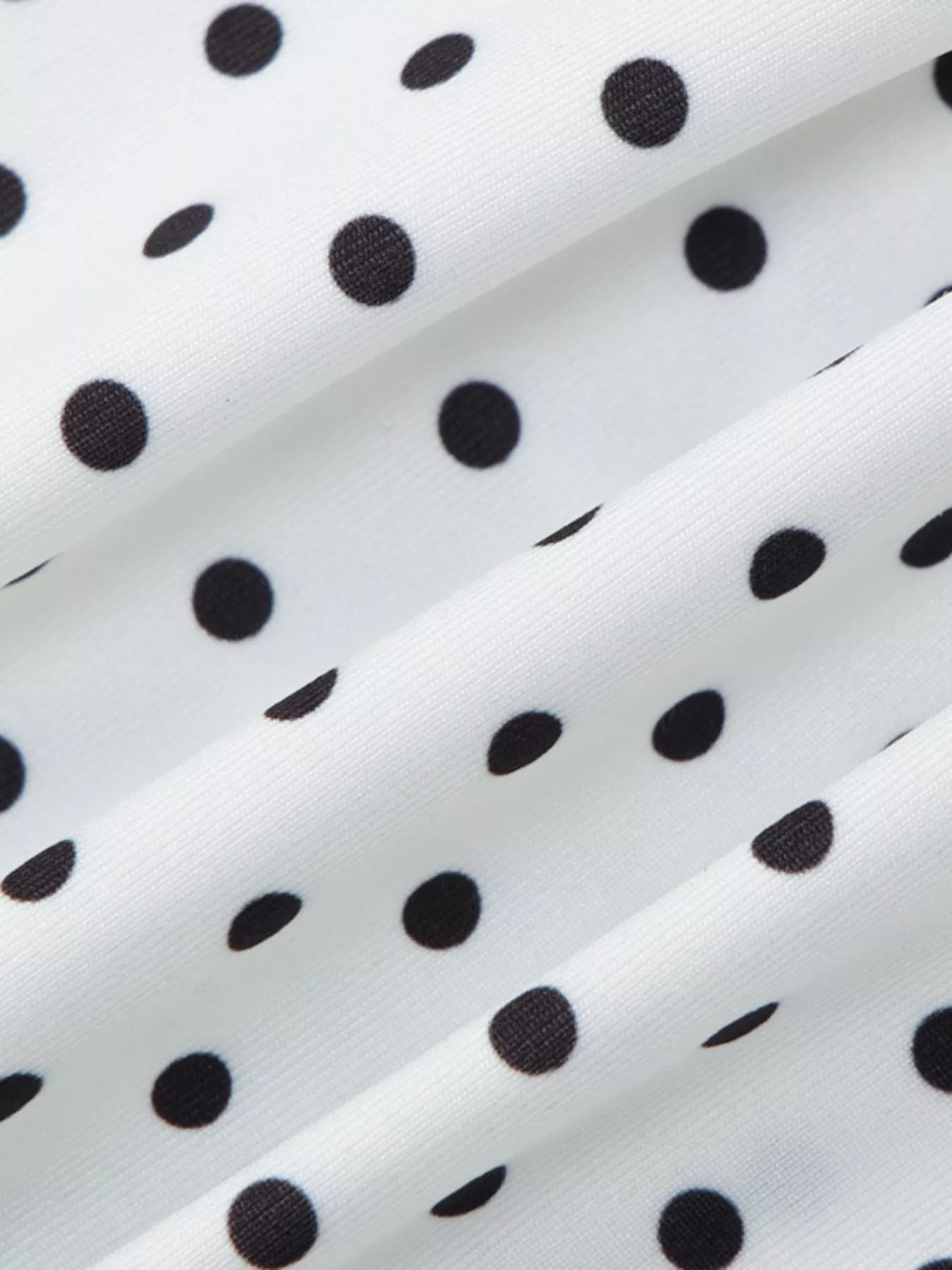 Close-up detail of white fabric with black polka dots from the ruched V-neck top
