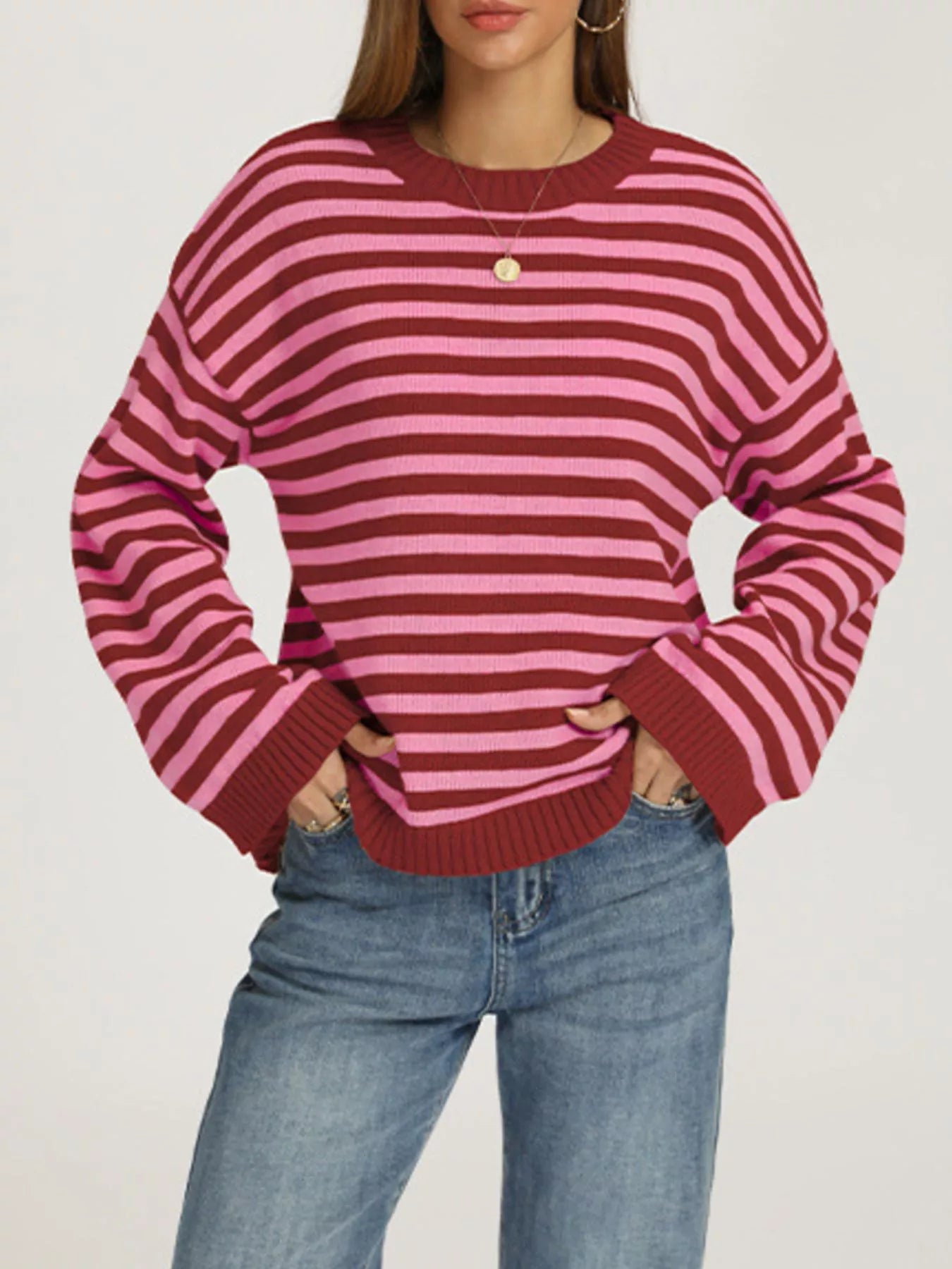 Front view of a red and pink striped dropped shoulder sweater with ribbed cuffs worn with jeans.