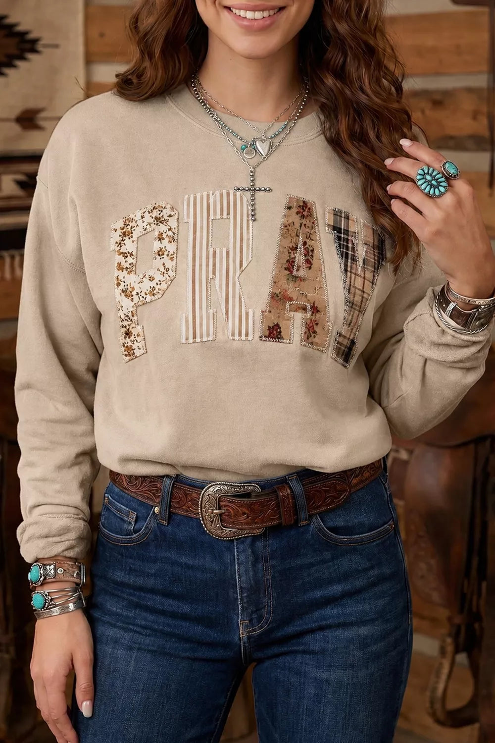 Khaki western sweatshirt with patchwork PRAY lettering worn with jeans, front view