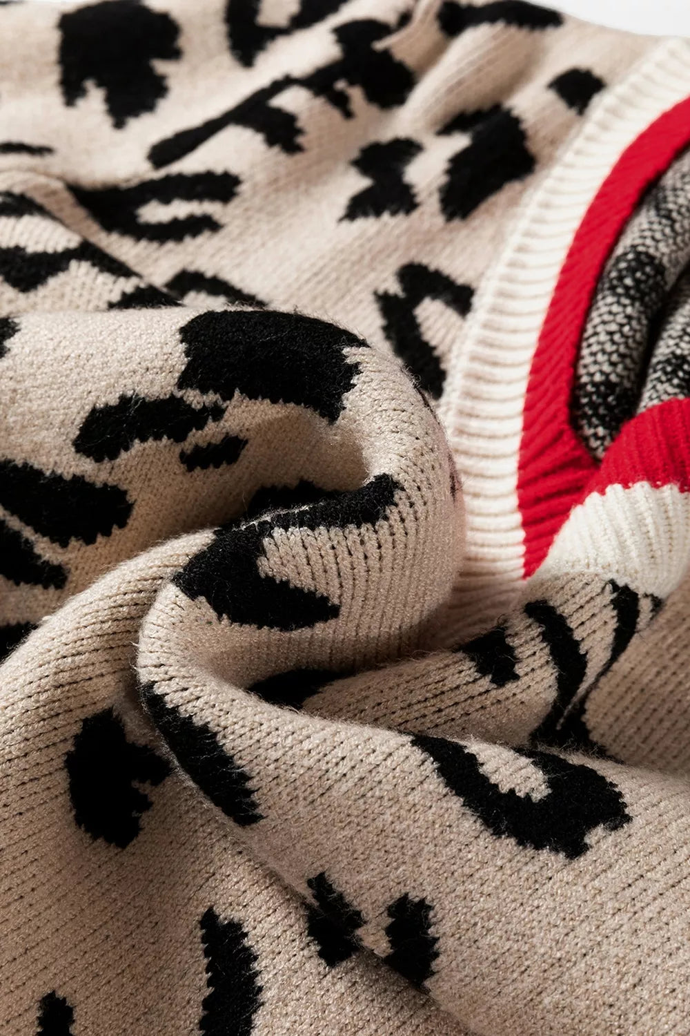 Close view of beige and black leopard knit fabric folded beside red ribbed trim.