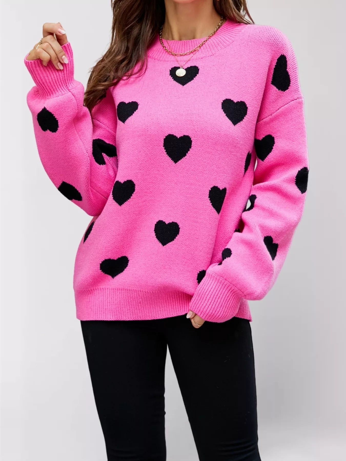 Front view of the hot pink dropped shoulder sweater with black hearts, one arm raised.