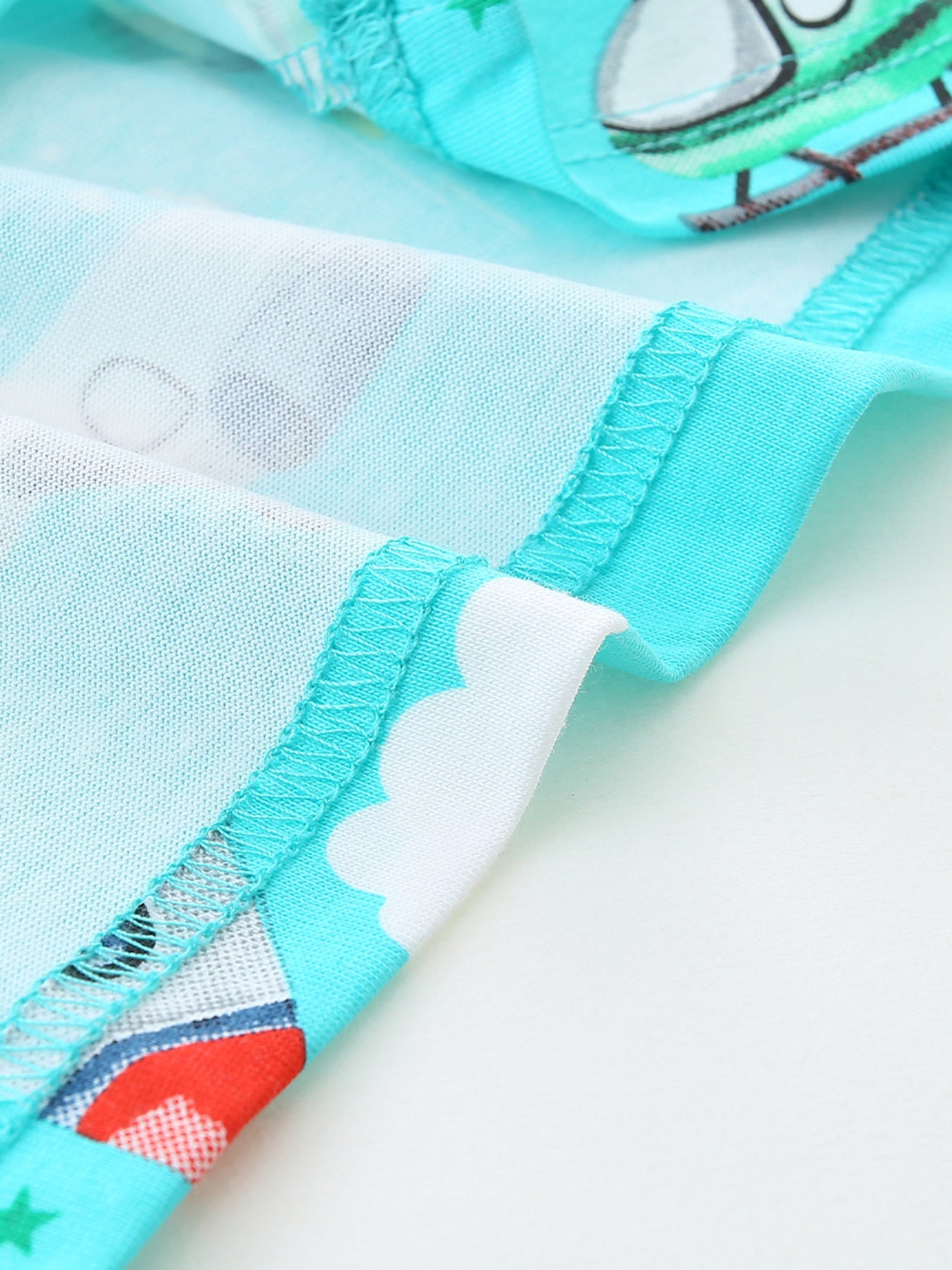 Close-up hem detail showing aqua stitching and a cloud print at the fabric edge