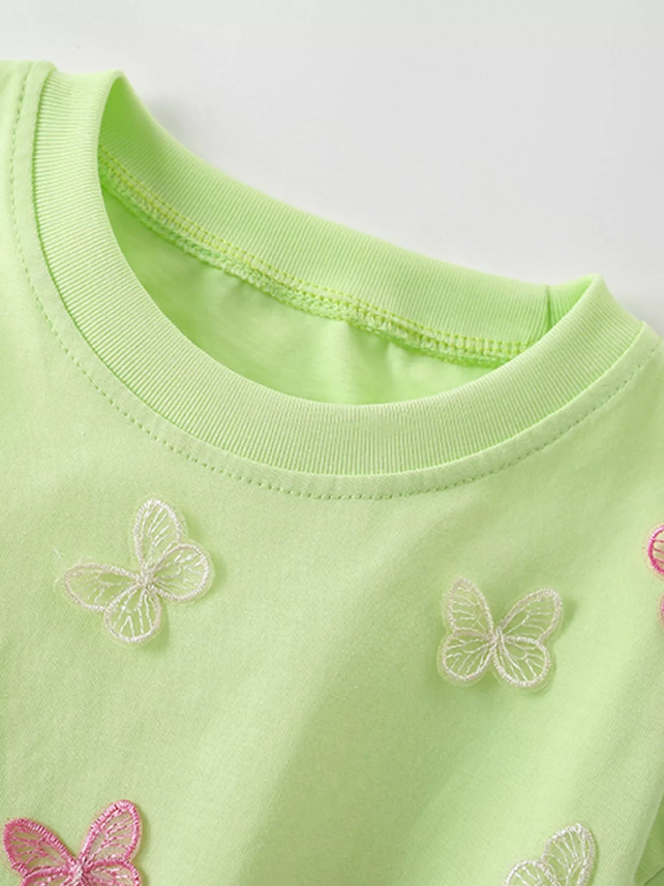Close view of the light green children's tee neckline with white butterfly appliques below it