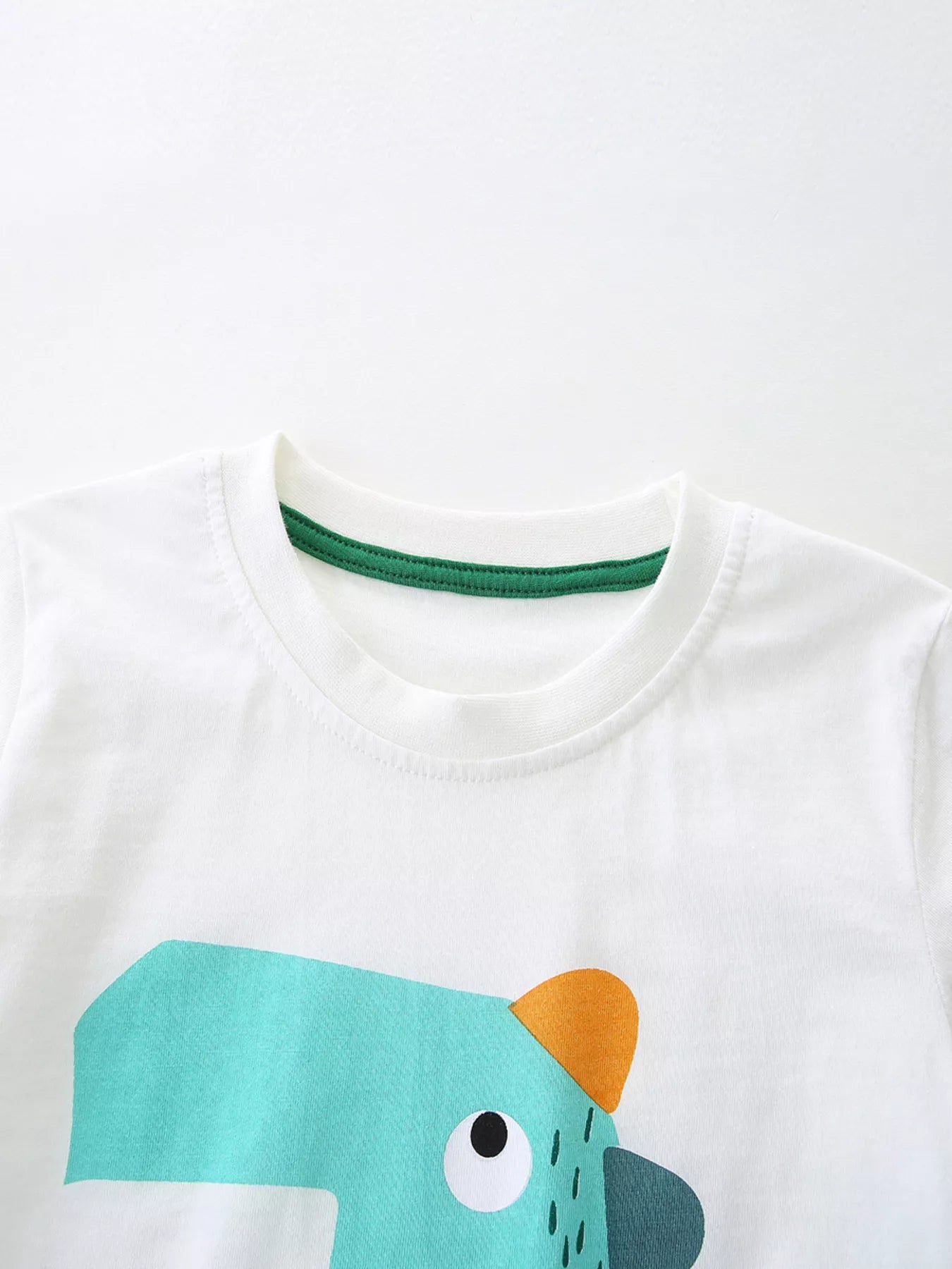 Close-up of white round neckline with green trim above the turquoise cartoon dinosaur graphic