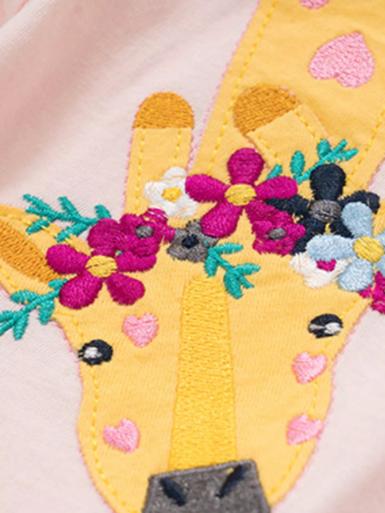 Close-up detail of the embroidered giraffe head with colorful flowers and pink hearts