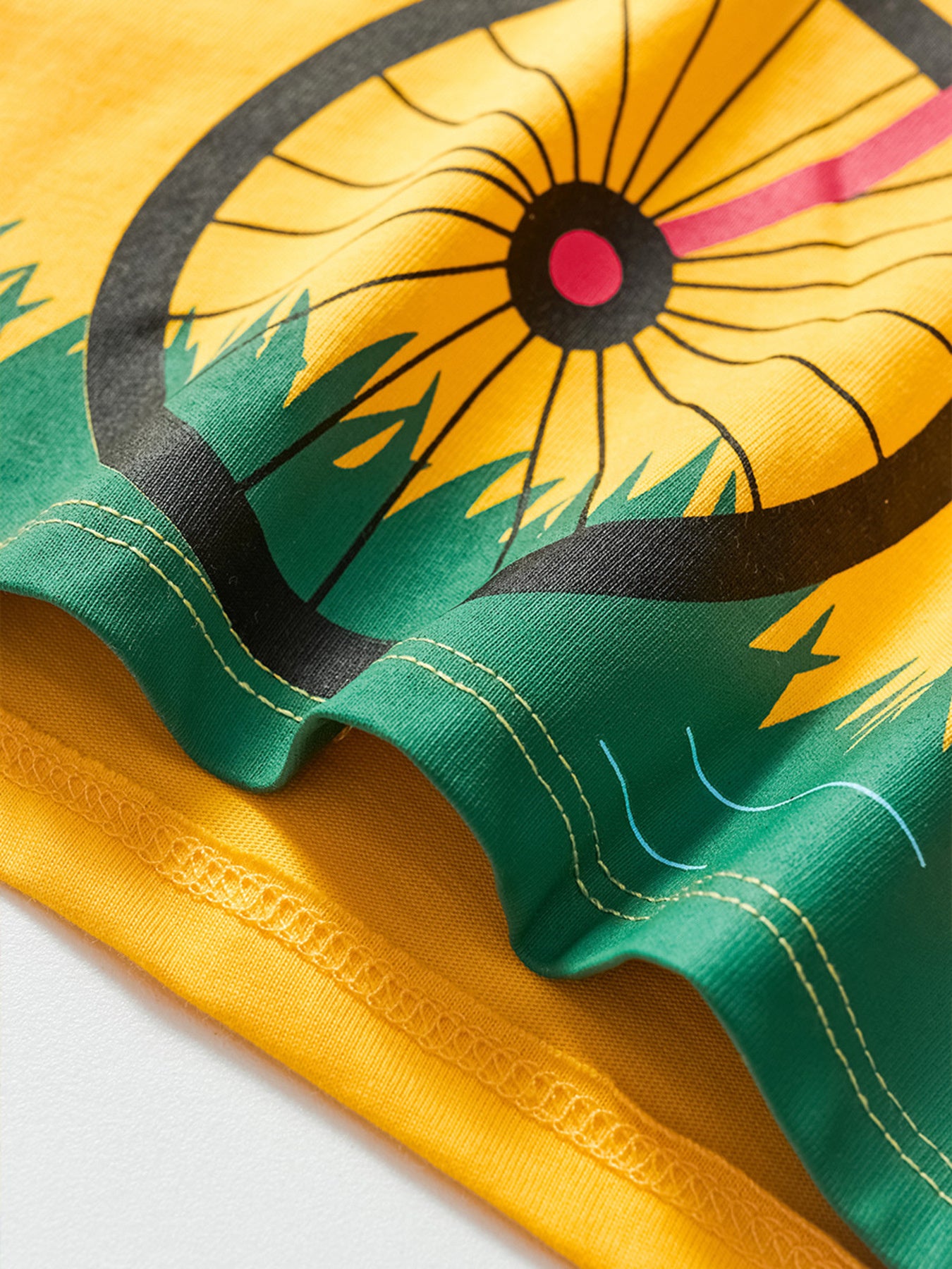 Close-up of yellow children's t-shirt hem with bicycle wheel and green grass print