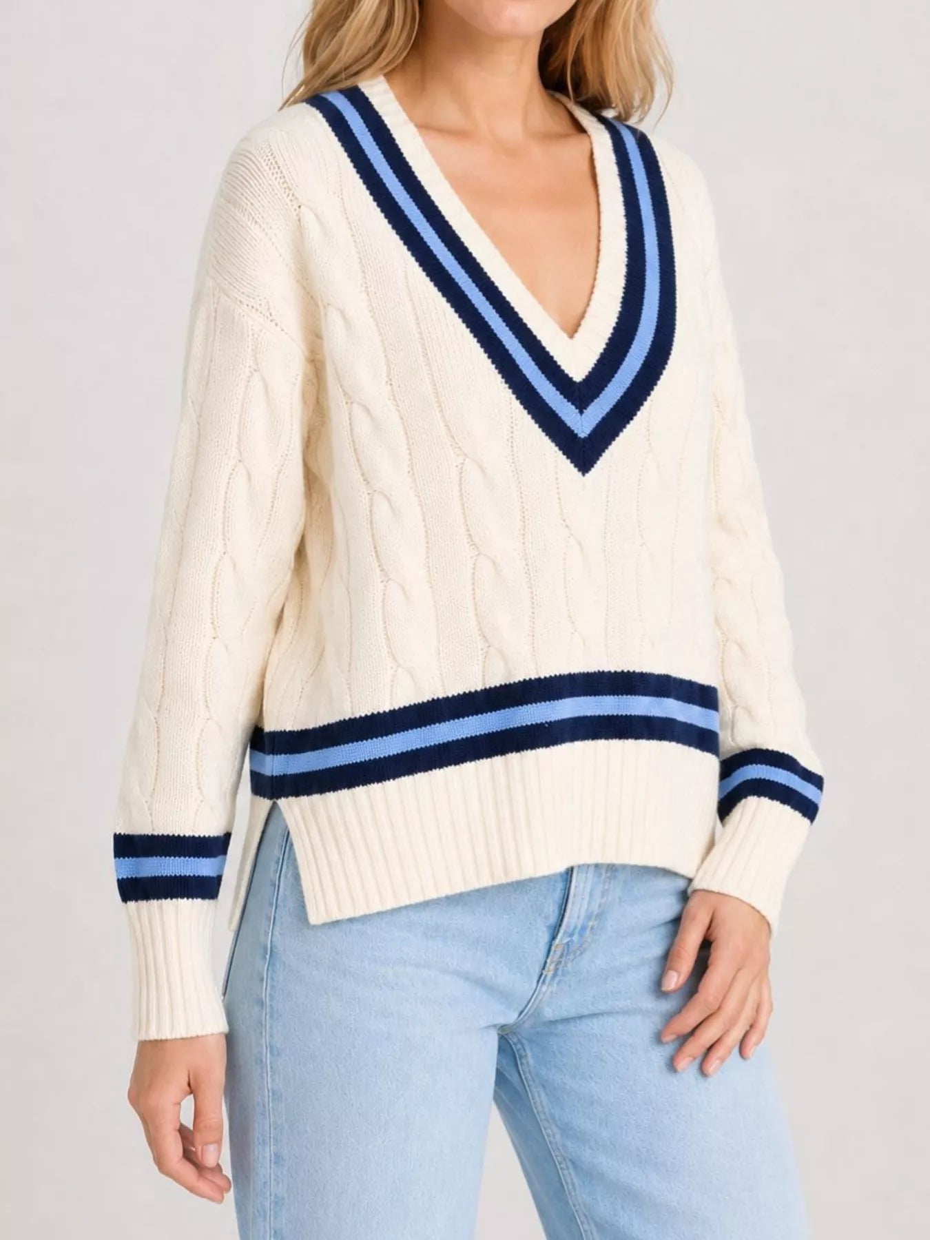 Side front view of a cream cable knit sweater with navy striped trim and side slit