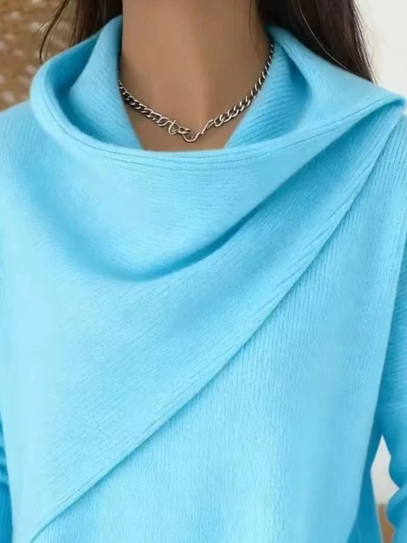 Close-up of the light blue cowl neckline showing the draped asymmetric collar and fine knit texture
