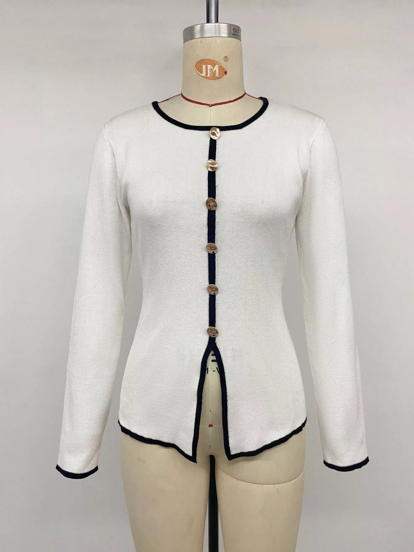 Front view of white knit top on a mannequin, with black trim and gold buttons.