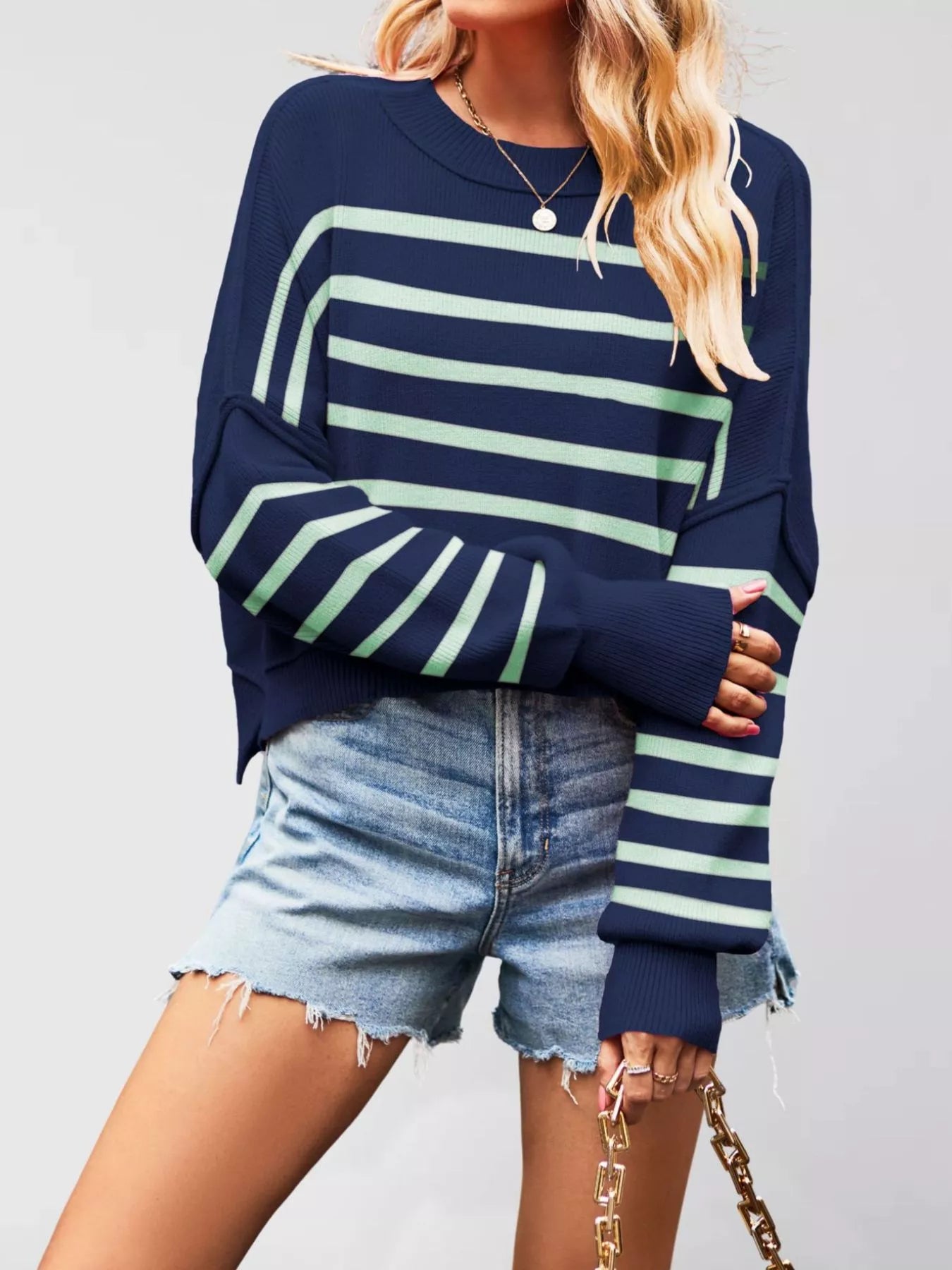Front view of a navy sweater with mint stripes, crew neck, and dropped shoulders worn with denim shorts.