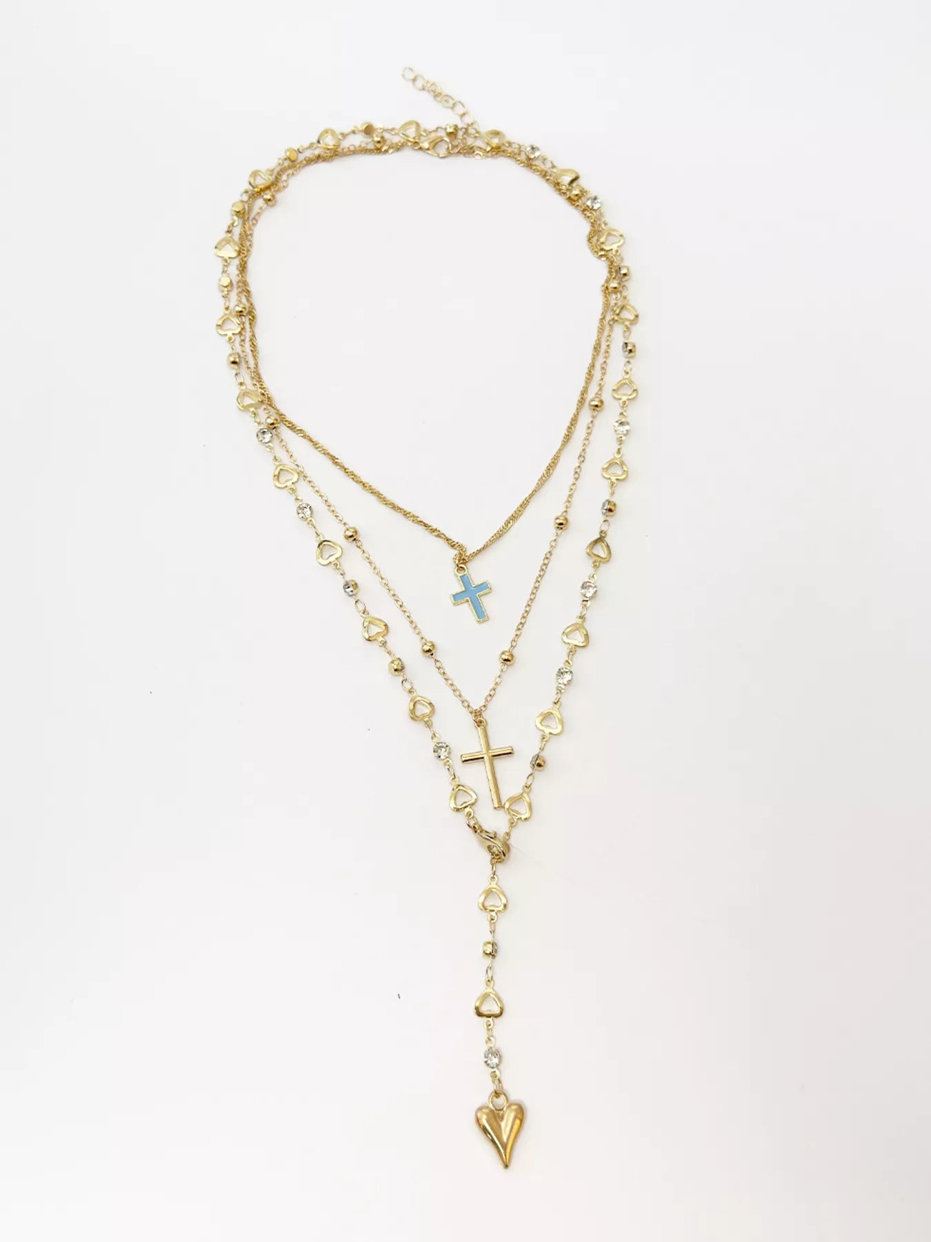 Layered gold necklaces laid flat on white background with blue cross and heart pendant