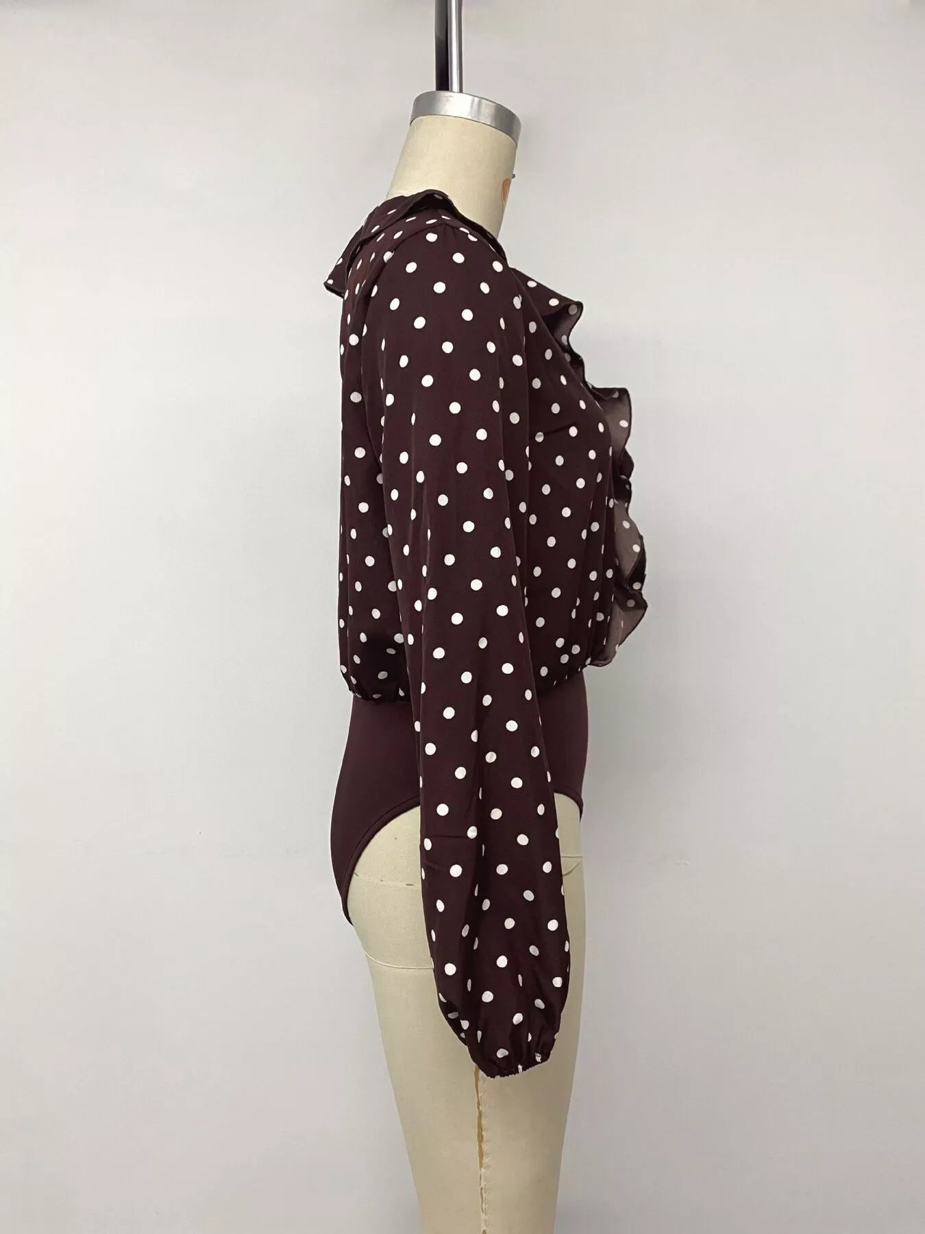 Mannequin side view of a coffee brown polka dot bodysuit with long sleeves
