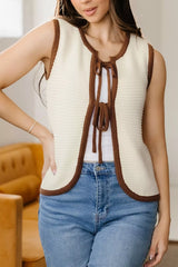 On-model front view of a beige tie front sweater vest with brown contrast trim