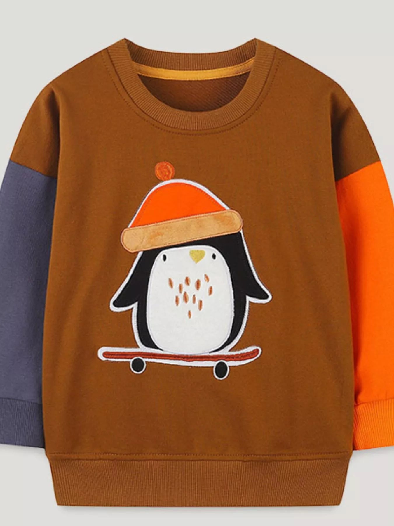 Flat lay front view of a children's caramel sweatshirt with a penguin on a skateboard and color blocked sleeves
