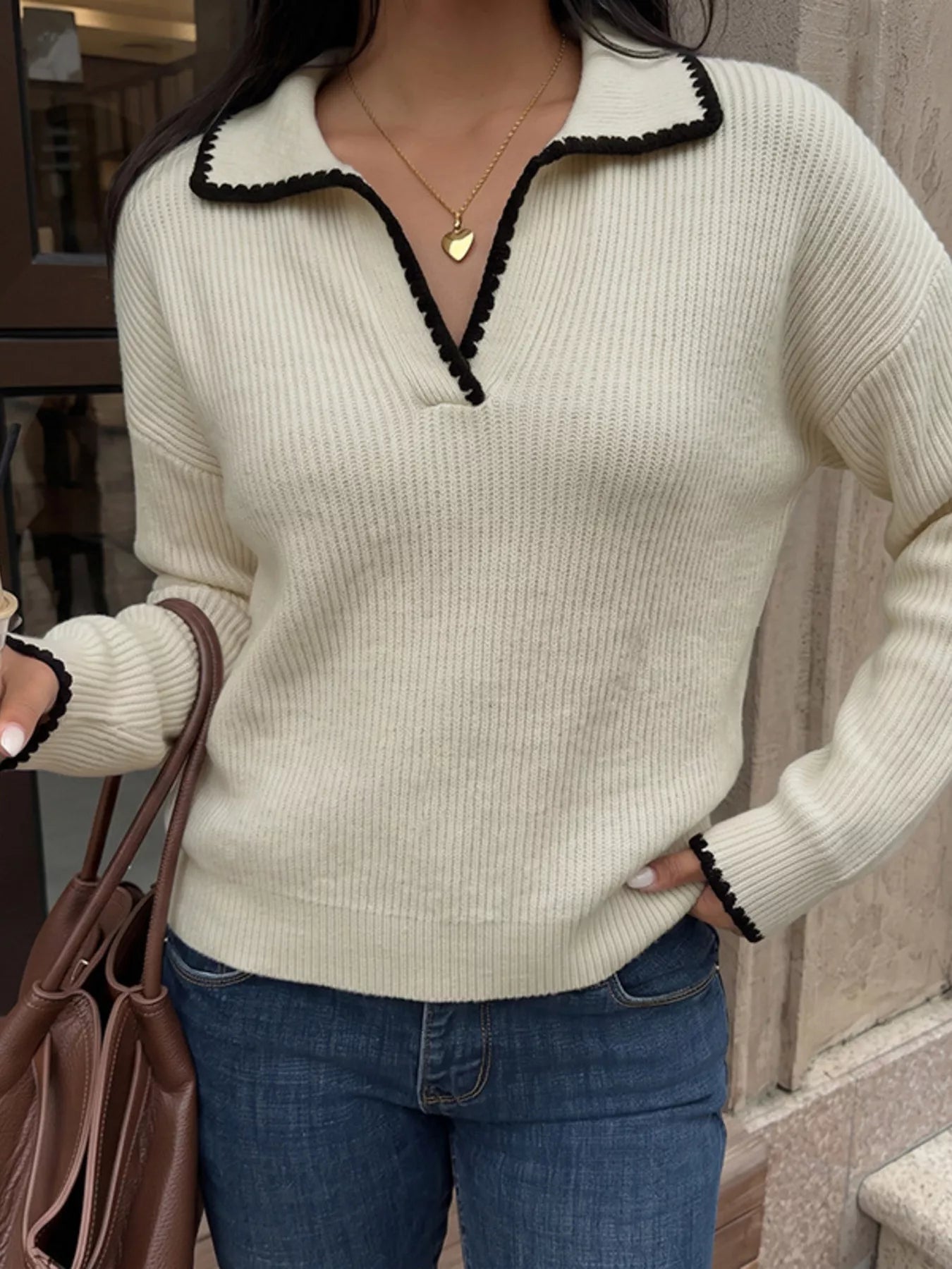Front view of a cream ribbed sweater with black scalloped trim on collar and cuffs