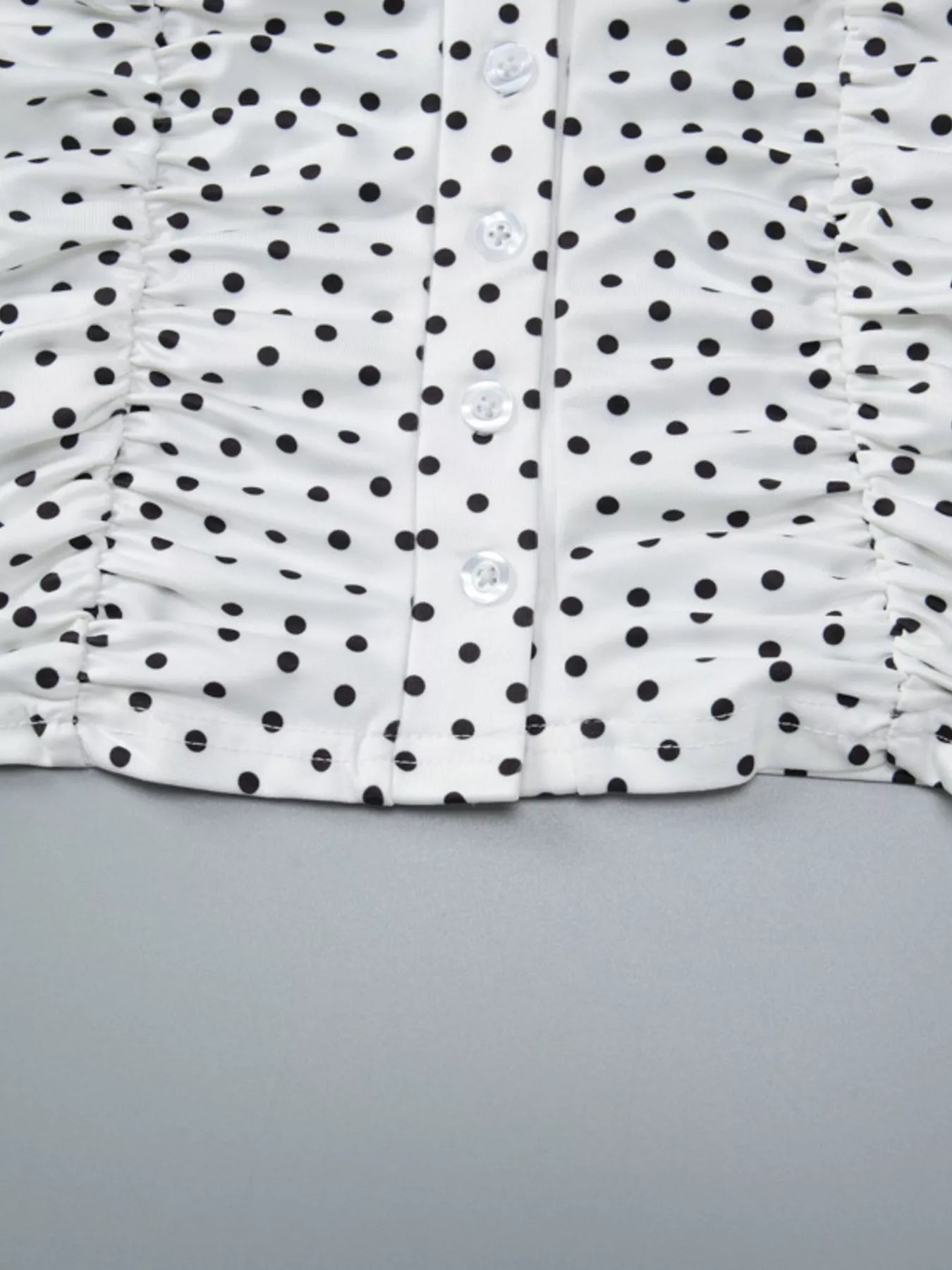 Close-up detail of white polka dot top showing ruched sides, V-neck seam, and front buttons