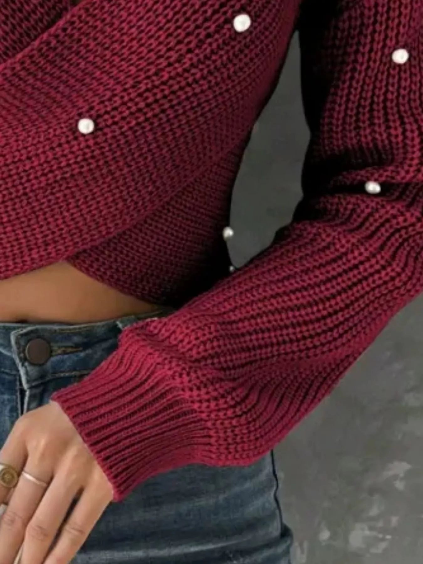 Close view of the burgundy crisscross sweater sleeve and pearl details