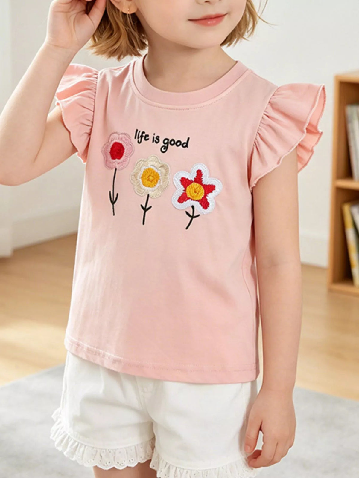 Blush pink children's ruffle sleeve t-shirt with embroidered flowers and lettering worn indoors