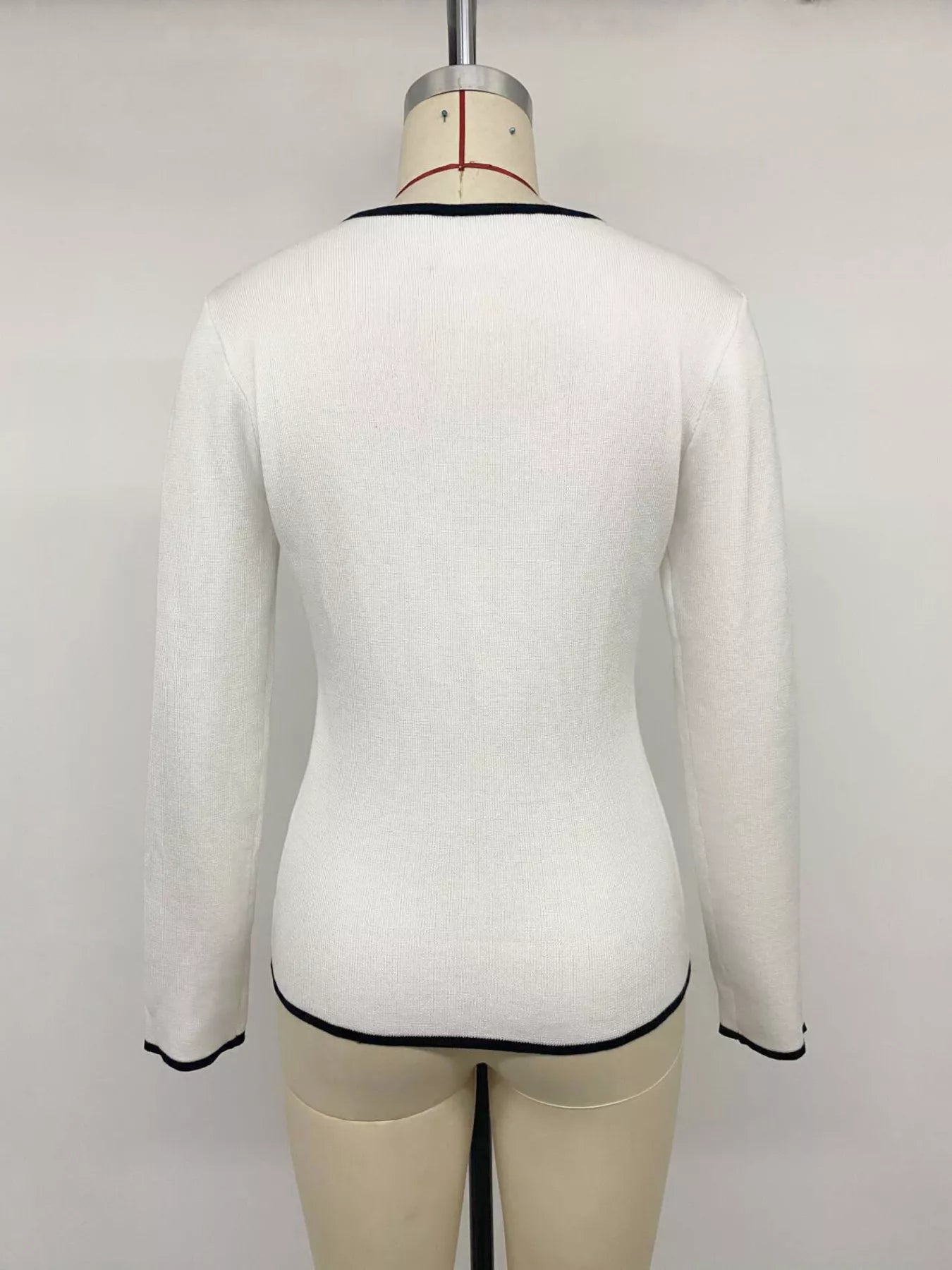 Back view of white knit top on a mannequin, with black trim at neckline and hem.