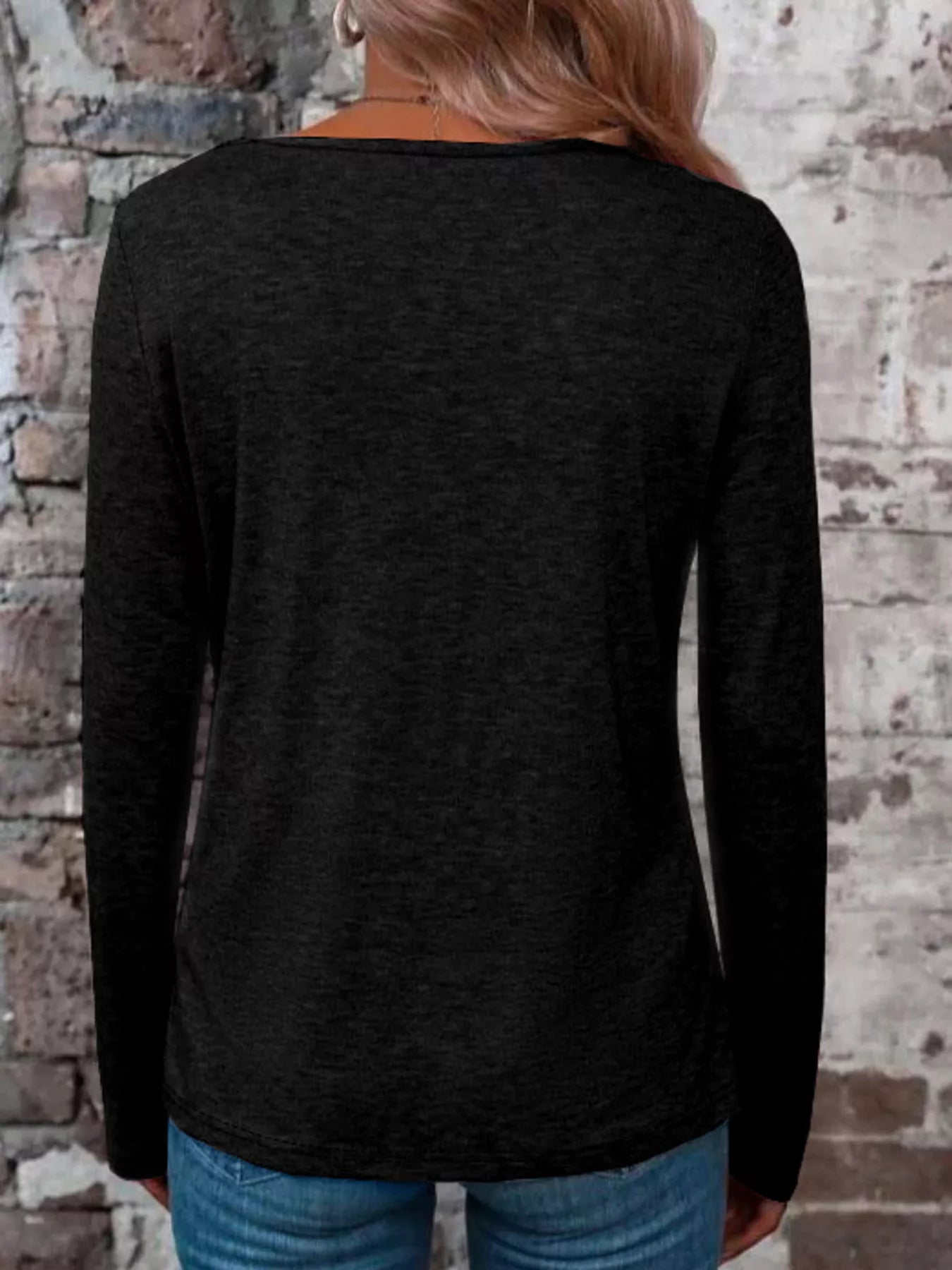 Back view of a black long-sleeve top with a wide neckline, styled with blue jeans.