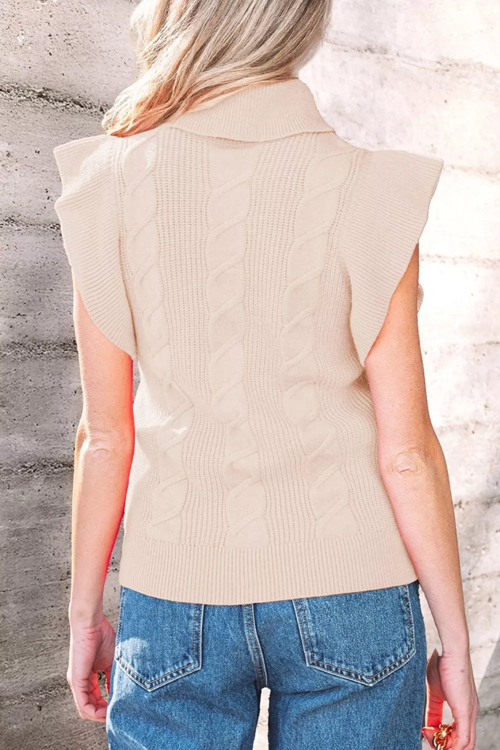 Back view of a beige cable knit turtleneck sweater with ruffled short sleeves