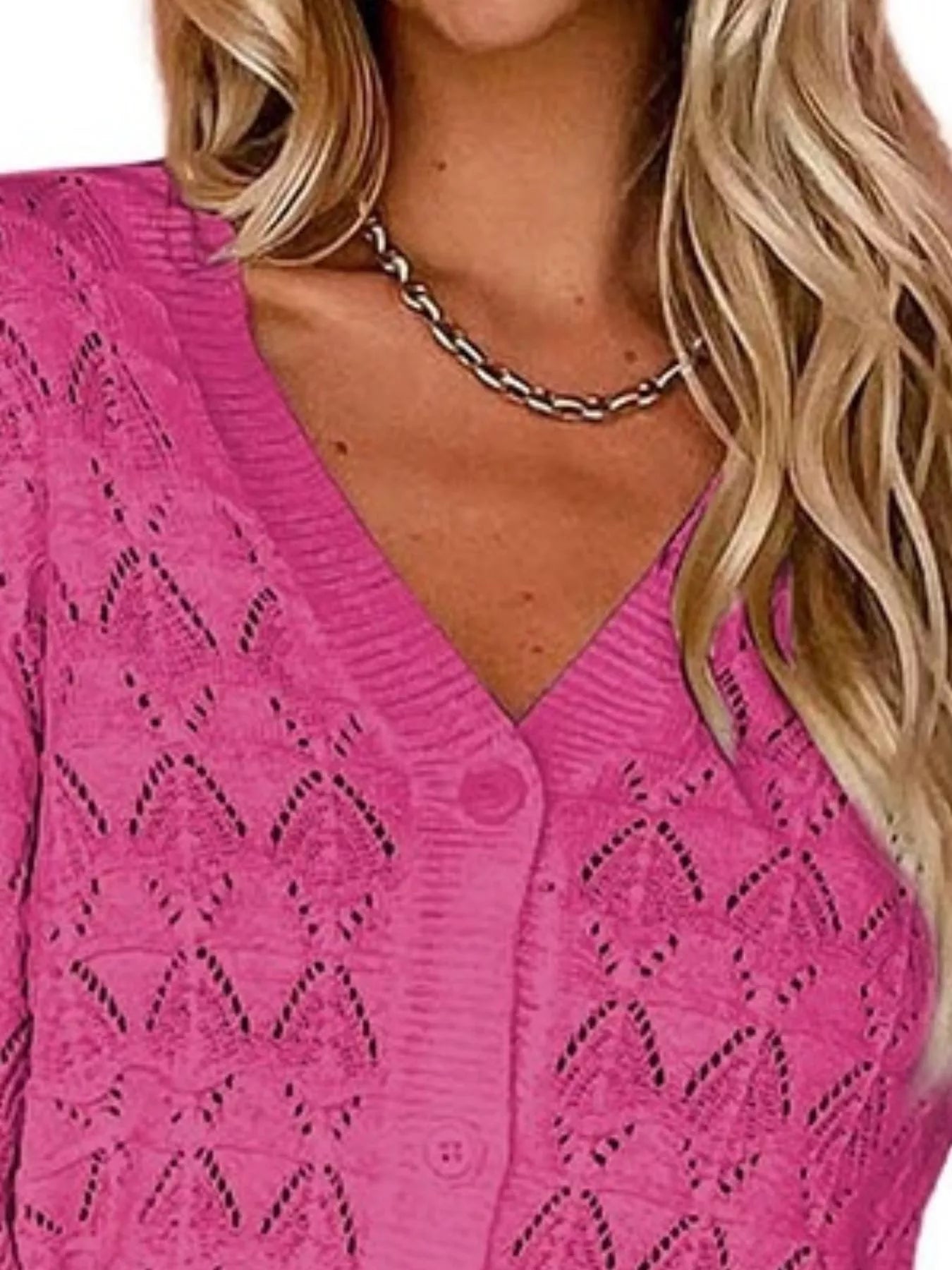 Close view of bright pink openwork knit cardigan showing V neckline and button front.