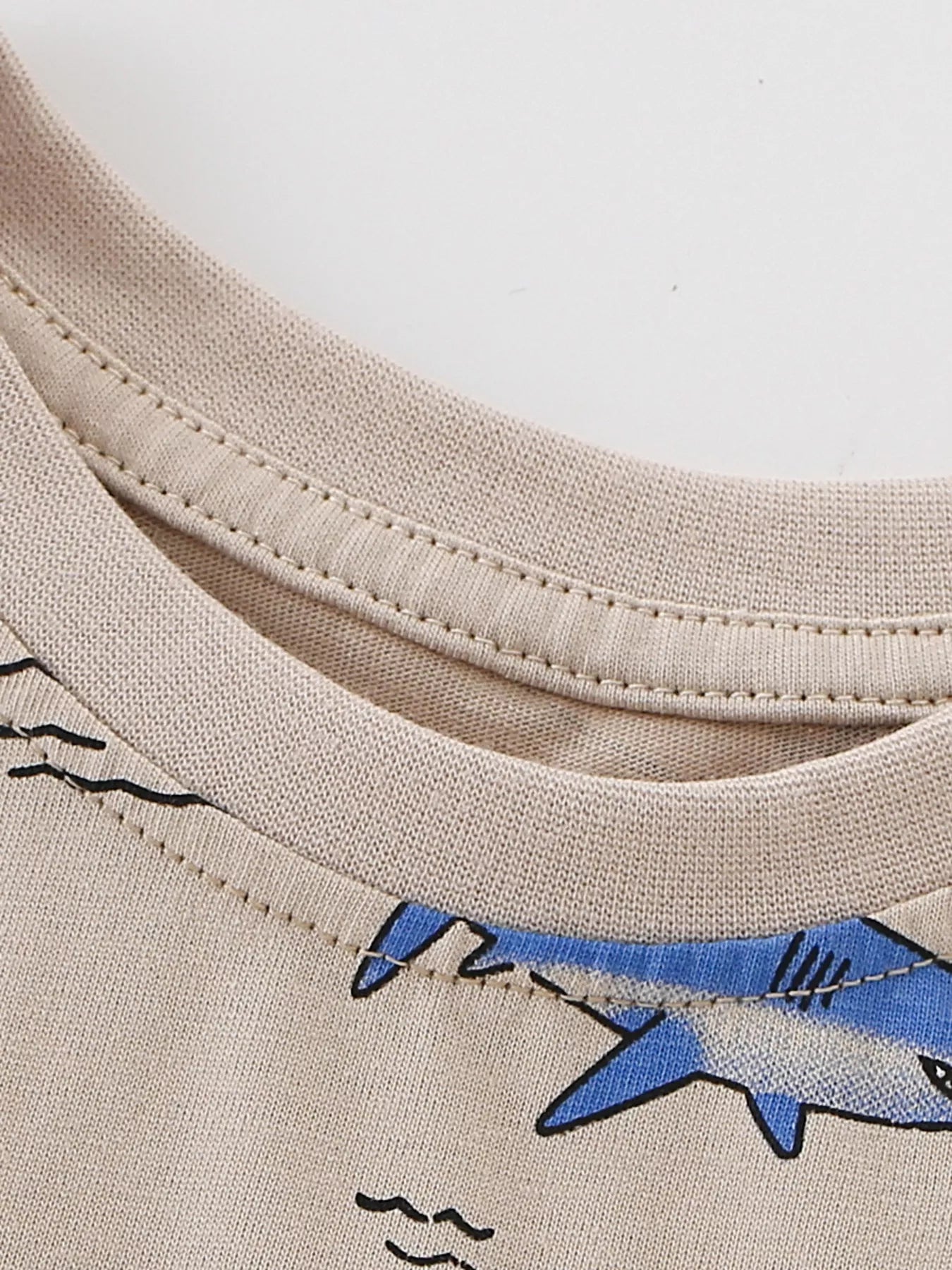 Close-up of ribbed crew neckline and shark print edge on tan children's tee