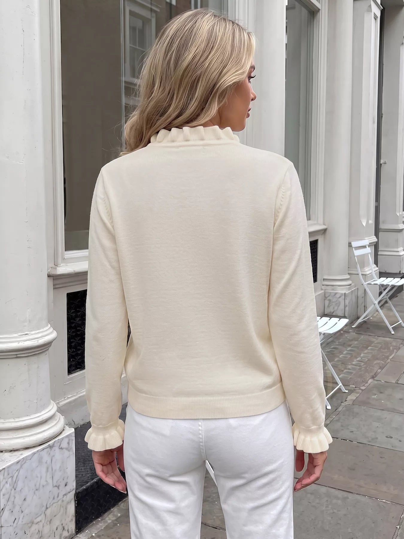 Back view of cream V neck knit top with ruffle cuffs and white pants