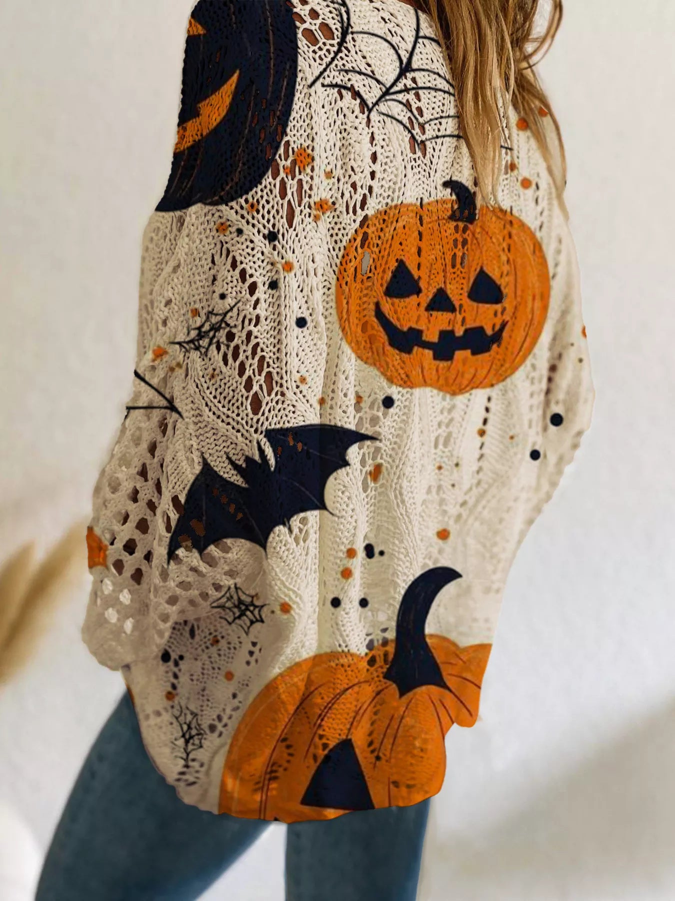 Close up side view of the beige openwork knit cover up with orange jack o lanterns and bats.