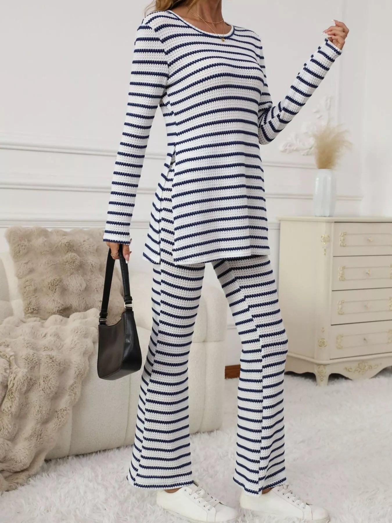 Women's blue and white striped long sleeve top and flared pants set, standing with a black handbag, side slit visible.