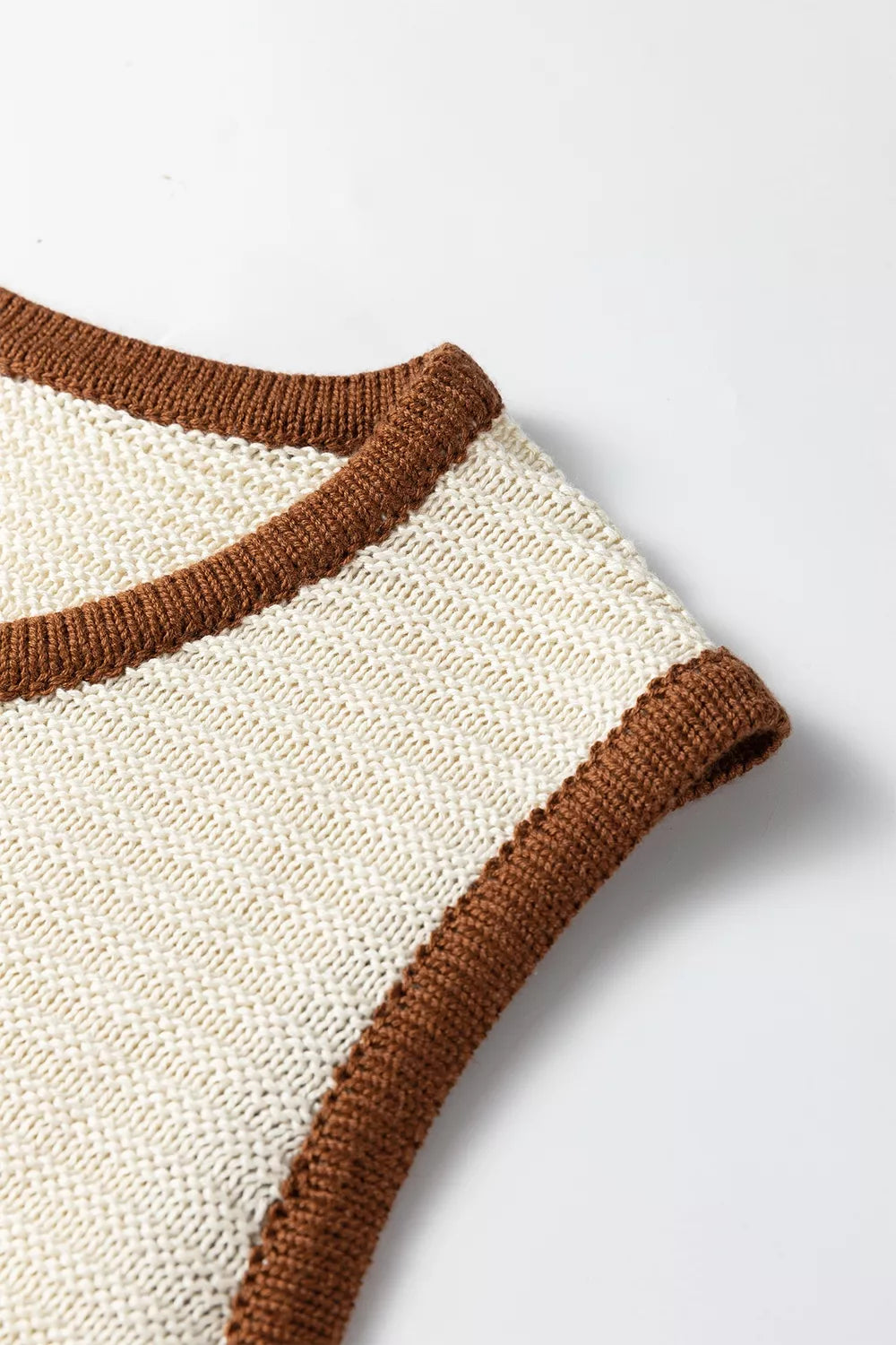 Close up detail of a beige sweater vest armhole with brown contrast trim and knit texture