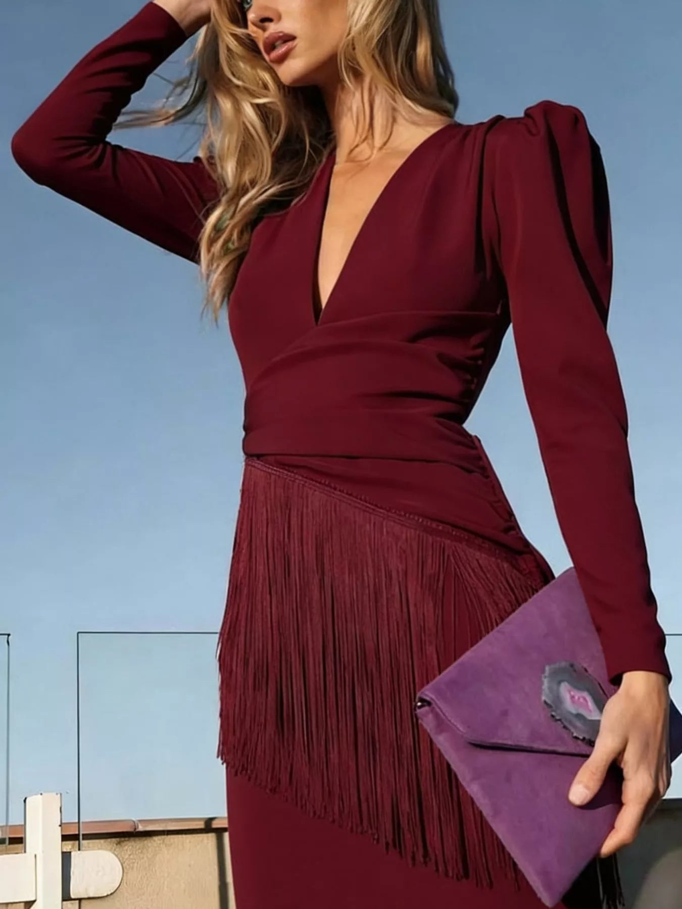 Close front view of a burgundy fringed maxi dress with a deep neckline and purple clutch