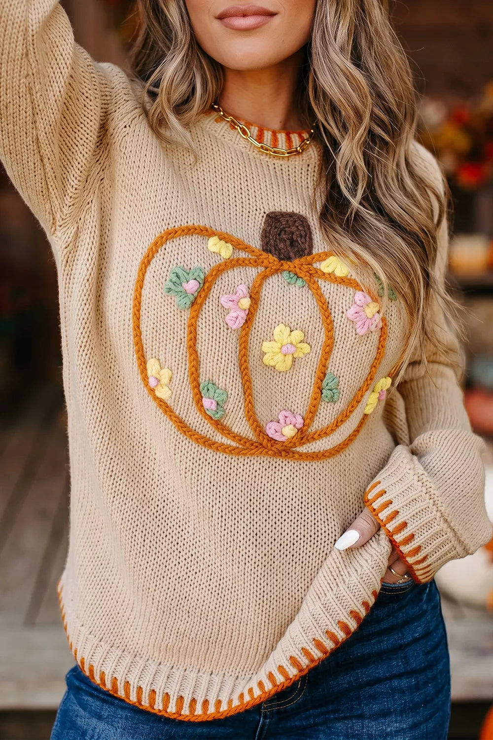 Close-up front view of a beige knit sweater with a floral embroidered orange pumpkin design