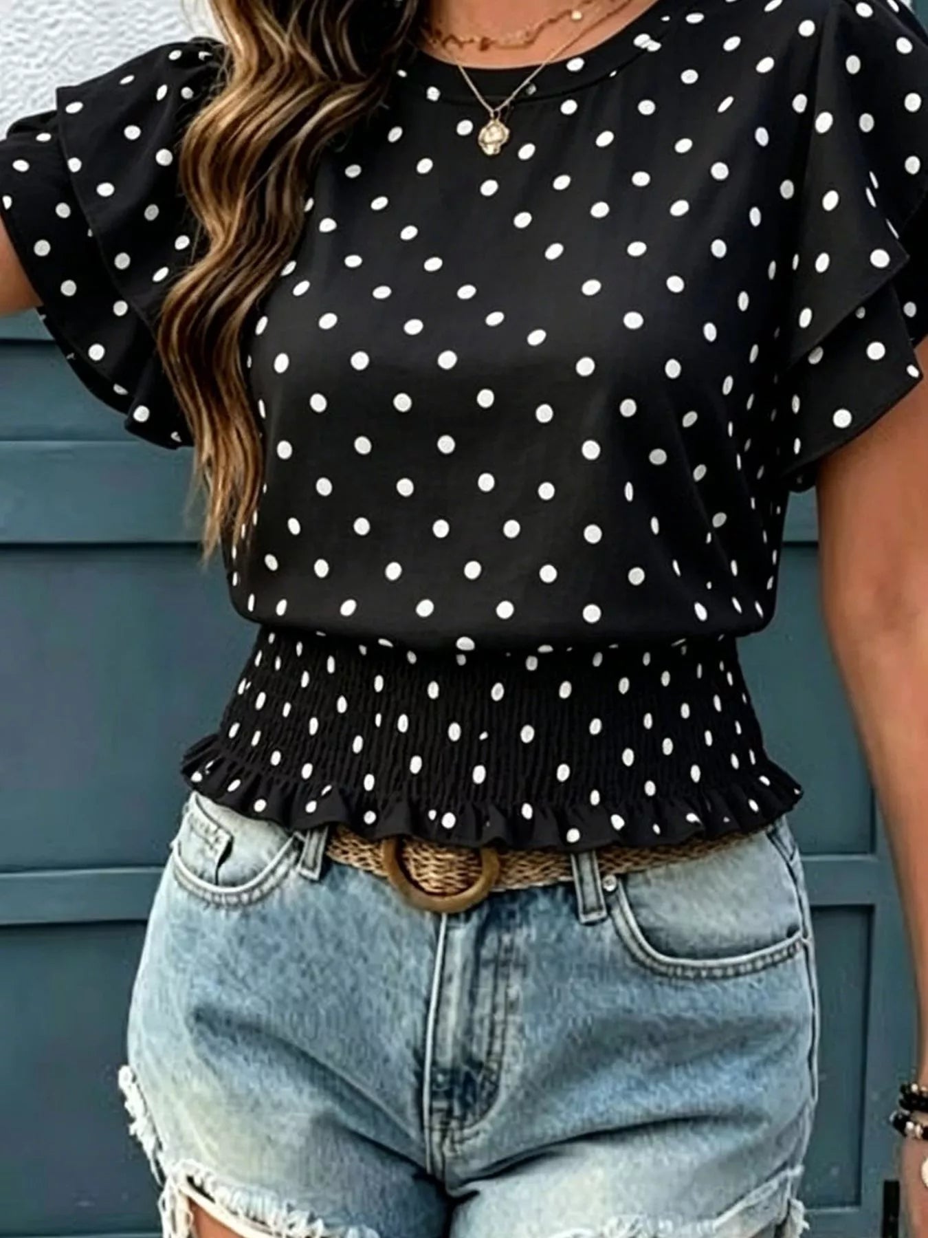 Black polka dot blouse with ruffled sleeves and peplum hem, shown styled with jeans and a woven belt